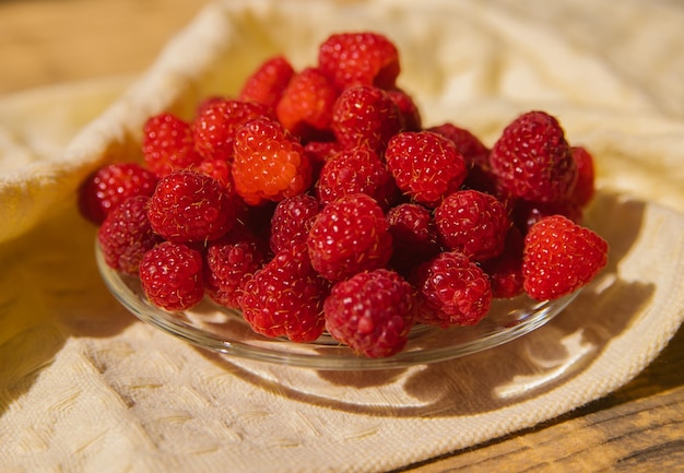 Raspberry fruits on a small saucer a bunch of summer berries on a wooden background Summer background Juicy appetizer or dessert