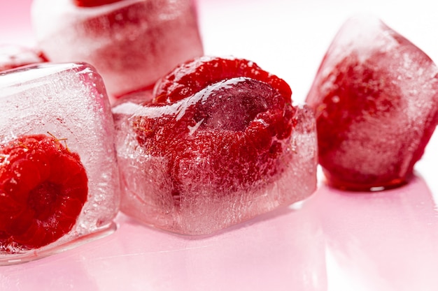 Raspberry ice cubes on pink glossy background