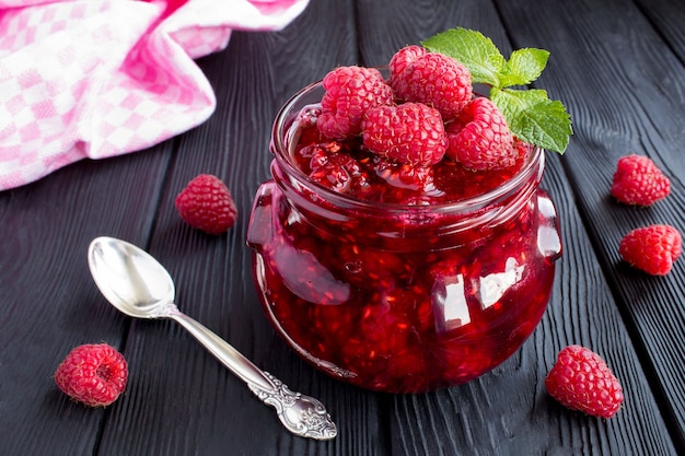 Raspberry jam in the glass jar on the black wooden