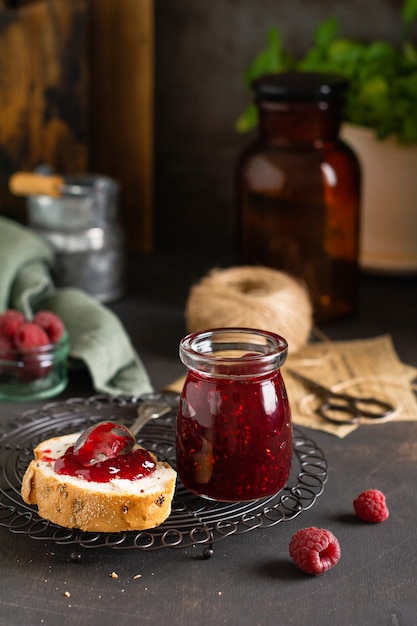 Photo raspberry jam in glass jar and sandwich with fresh raspberry berries on the old retro background