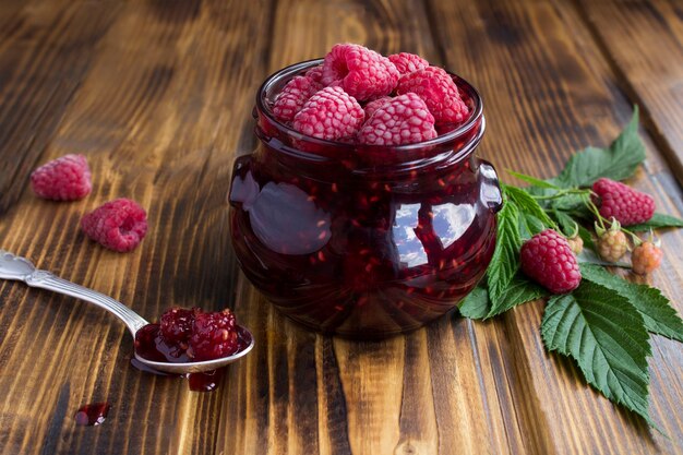 Raspberry jam in the glass jar on the wooden table