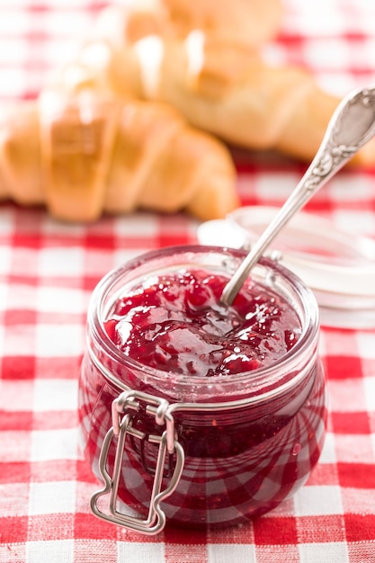 Photo raspberry jam jelly in jar on checkered tablecloth