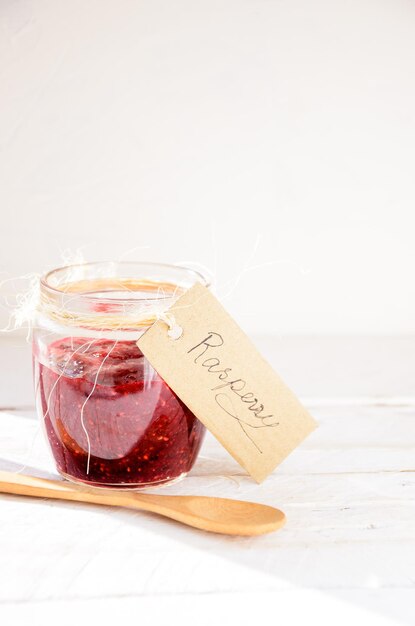 Raspberry jam on a white rustic background and wooden spoon