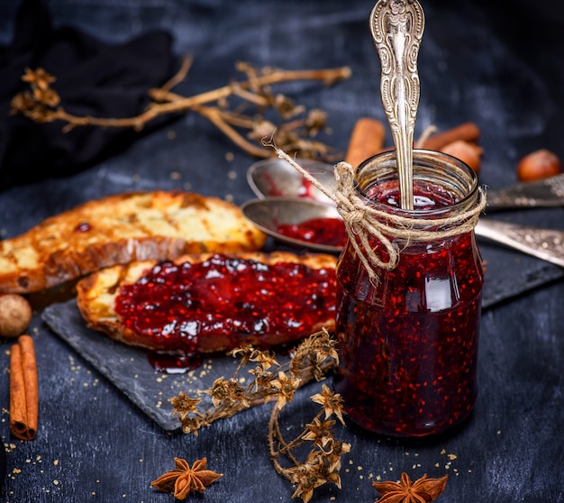 Raspberry jam with a glass jar and slices of white bread 