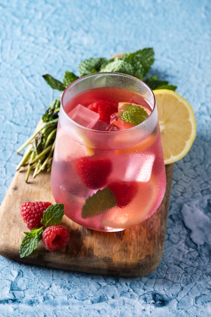 Raspberry lemonade drink in glass on blue background