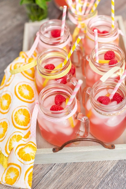 Photo raspberry lemonade garnished with fresh lemon and raspberries in drinking mason jars.