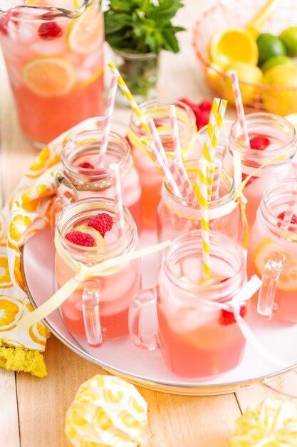 Raspberry lemonade garnished with fresh lemon and raspberries in drinking mason jars.