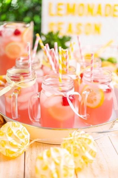 Raspberry lemonade garnished with fresh lemon and raspberries in drinking mason jars.