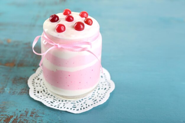 Raspberry milk dessert in glass jar on color wooden background