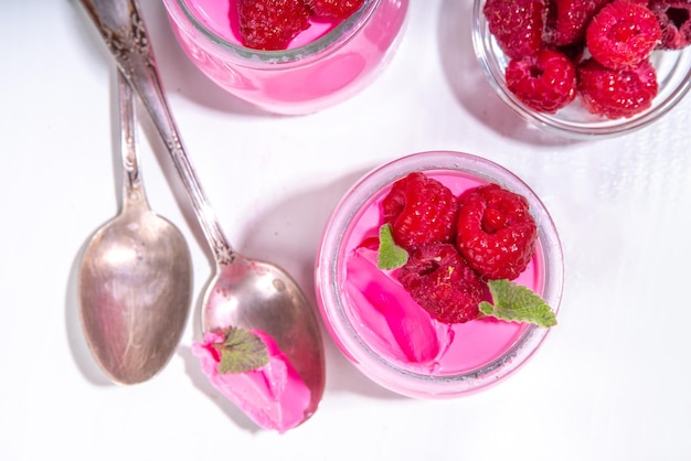 Raspberry panna cotta dessert with fresh raspberries and melissa mint leaves Pink panna cotta in small portion jars on a white background
