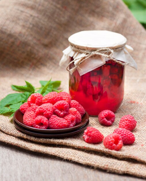 Raspberry preserve in glass jar and fresh raspberries on a plate