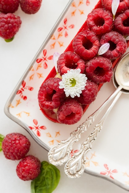 Foto raspberry tartlet versierd met bloemen op een bord met antieke lepels witte achtergrond