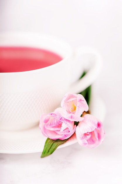 Raspberry tea and pink freesia flowers on a white wall, copy space