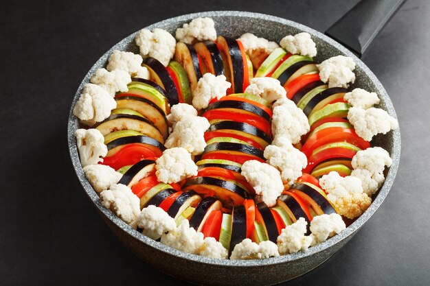 Ratatouille of freshly cut vegetables in a frying pan on a dark\
background . traditional french vegetable dish