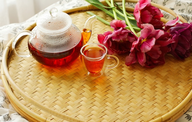 On a rattan round tray, there is a cup, a teapot, and tulips. the concept of breakfast in bed.