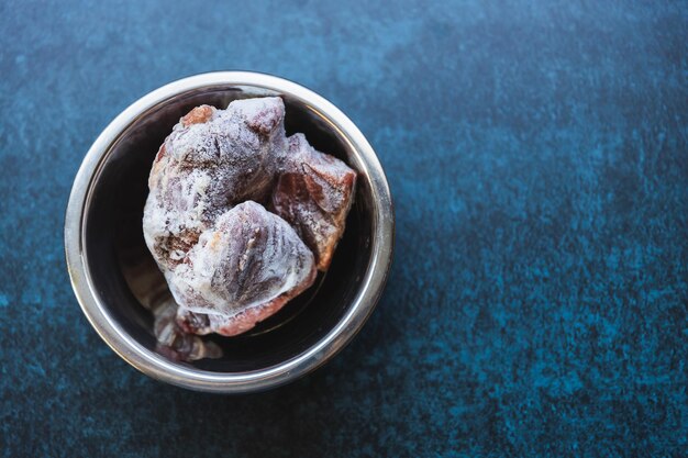 Rauw bevroren vlees in een metalen kom op een blauwe achtergrond Eten en drinken concept