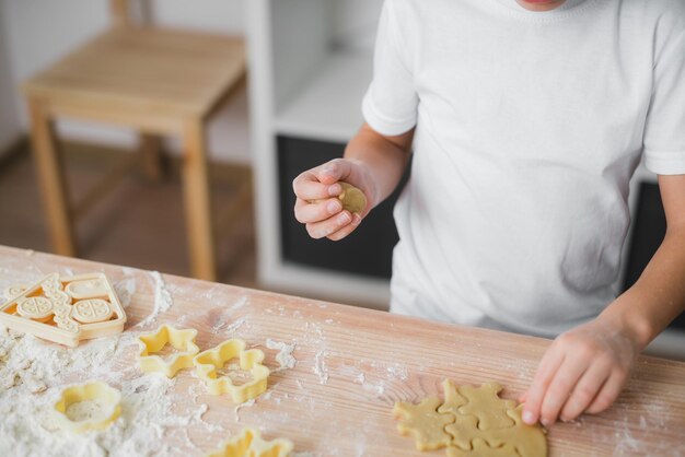 Rauw deeg in de handen van een kind dat koekjes in de keuken bereidt.