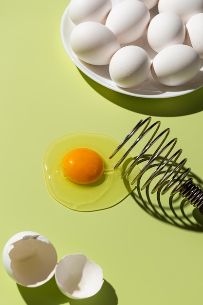 Foto rauw eigeel gebroken op een groene achtergrond naast de schaal en een bord eieren