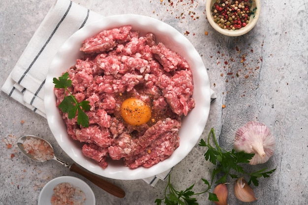 Rauw gehakt vlees gemalen vlees rundvlees varkensvlees of lam kruiden kruiden en eieren op witte plaat op lichtgrijze betonnen achtergrond Vers gehakt vlees klaar om te koken Voedsel koken achtergrond Bovenaanzicht