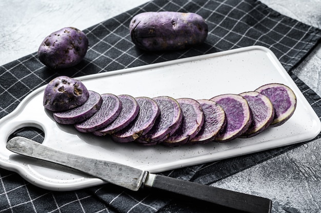 Rauw gesneden violet aardappelen op een witte snijplank. Grijze achtergrond. Bovenaanzicht