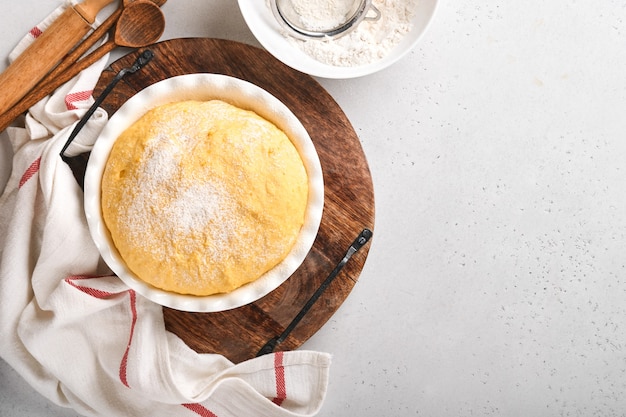 Rauw gistdeeg met pompoen in witte kom bedekt met een handdoek op de met bloem bestoven keukentafel, receptidee. concept thuis bakken van brood, broodjes of cinnabon of het maken van deeg.