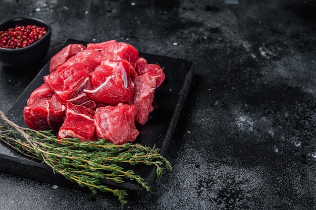 Rauw in blokjes gesneden rood rundvlees voor Goulash op marmeren bord. Zwarte achtergrond. Bovenaanzicht. Ruimte kopiëren.