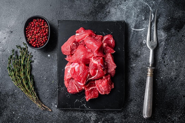 Rauw in blokjes gesneden rood rundvlees voor goulash op marmeren bord. zwarte achtergrond. bovenaanzicht.