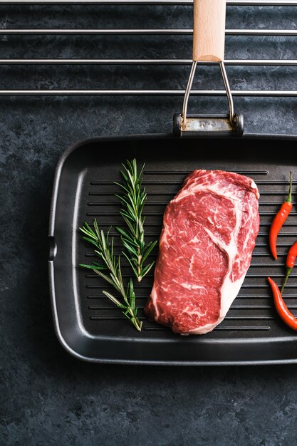 Rauw rib eye biefstuk op zwarte grillpan met chili peper en rozemarijn