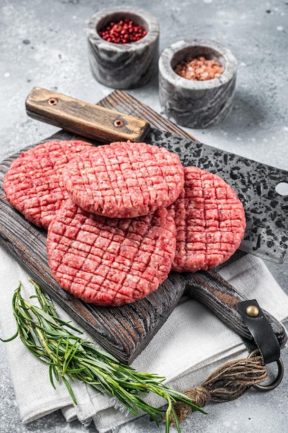 Rauw rundvlees vlees hamburger pasteitjes op slager houten bord met vlees hakmes grijze achtergrond bovenaanzicht