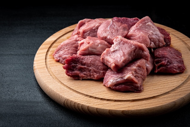 Rauw varkensvlees gesneden vlees op een houten bord op zwarte tafel.