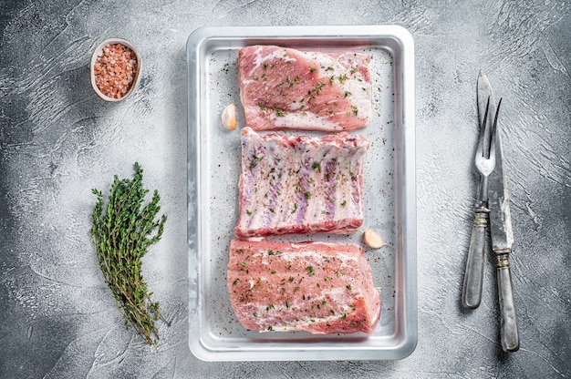 Rauw varkensvlees, lendenvlees, spareribs en borststuk op bakplaat. Witte achtergrond. Bovenaanzicht.