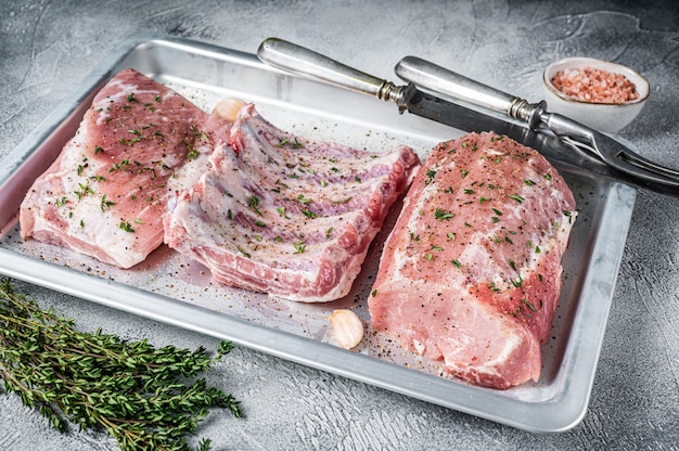 Rauw varkensvlees, lendenvlees, spareribs en borststuk op bakplaat.