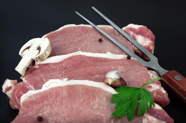 Rauw varkensvlees om te grillen en vleesvork bij het snijden van de keuken Stukken rauw rosbiefvlees met ingrediënten om te koken Vers rundvlees om te grillen