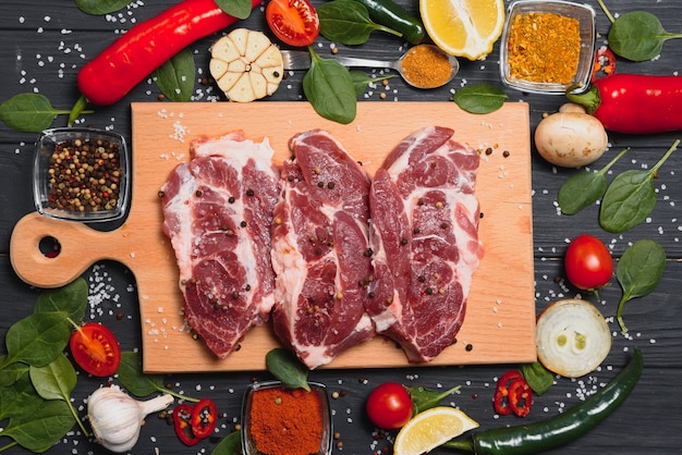 Rauw varkensvlees op houten snijplank aan de keukentafel voor het koken van varkensvlees steak geroosterd of gegrild met ingrediënten kruiden en specerijen, vers varkensvlees