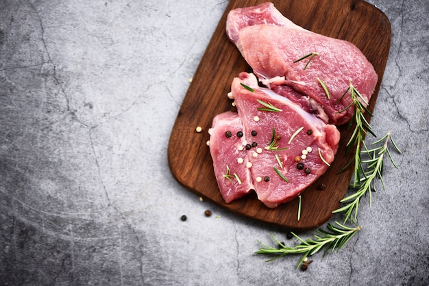 Rauw varkensvlees op houten snijplank aan keukentafel voor het koken van varkensvlees steak geroosterd of gegrild met ingrediënten kruiden en specerijen Vers varkensvlees