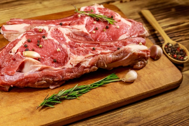 Rauw vers rundvlees rib eye steak op bot met kruiden, knoflook en rozemarijn op houten tafel