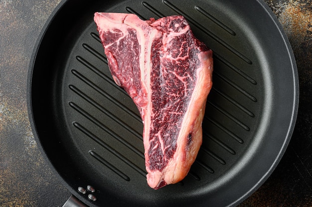 Rauw vers rundvlees t-bone steak drya leeftijd gesneden set, in gietijzeren pan, op oude donkere rustieke achtergrond, bovenaanzicht plat lag