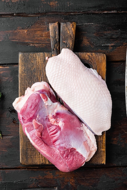 Rauw vers vlees, eendenborstfilet, op houten snijplank met oud slagersmes, op oude donkere houten tafel