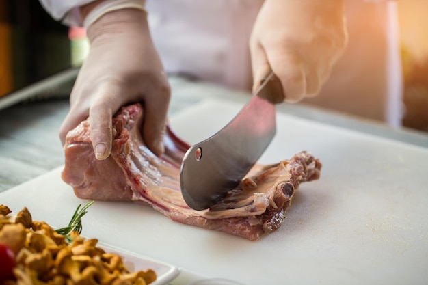 Rauw vlees met botten. Hand houdt een hakmes. Hoe kalfsribben te koken. Scherpste mes in de keuken.