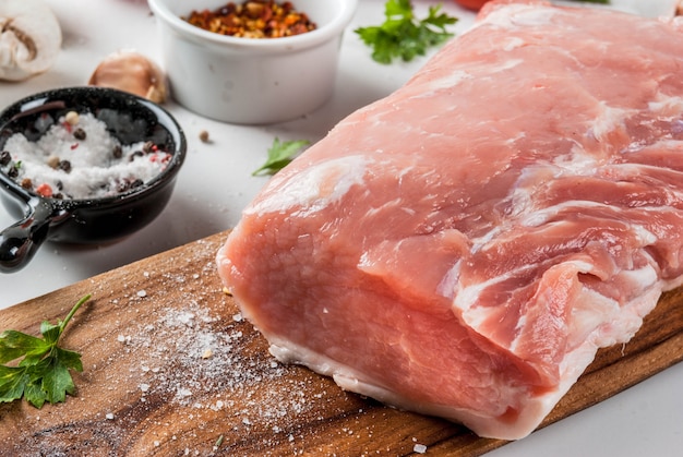 Rauw vlees met ingrediënten voor het diner. varkensfilet, ossenhaas, op snijplank, met zout, peper, peterselie, rozemarijn, olie, knoflook, tomaat, champignon. zwarte stenen tafel, kopie ruimte