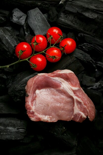 rauw vlees steak op een zwarte achtergrond van houtskool rauwe steak met cherrytomaatjes op de kolen