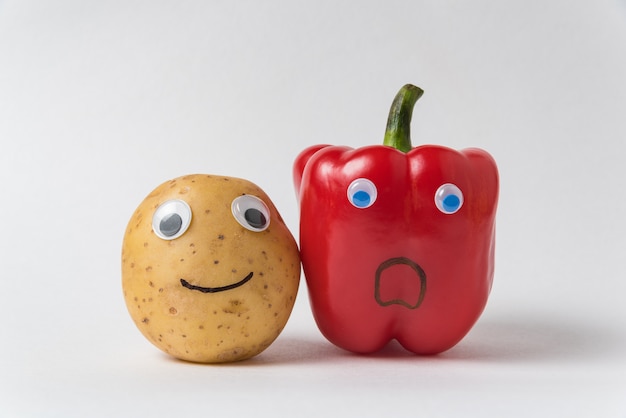 Rauwe aardappelen en rode paprika met grappige gezichten op witte achtergrond