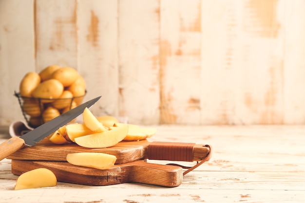 Rauwe aardappelen met mes en snijplanken op houten tafel