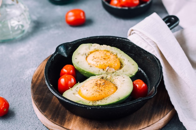 Rauwe avocado helften, klaar om te bakken, gevuld met ei en cherrytomaatjes in een pan op tafel. Gezond eten. Flexitarisch dieet