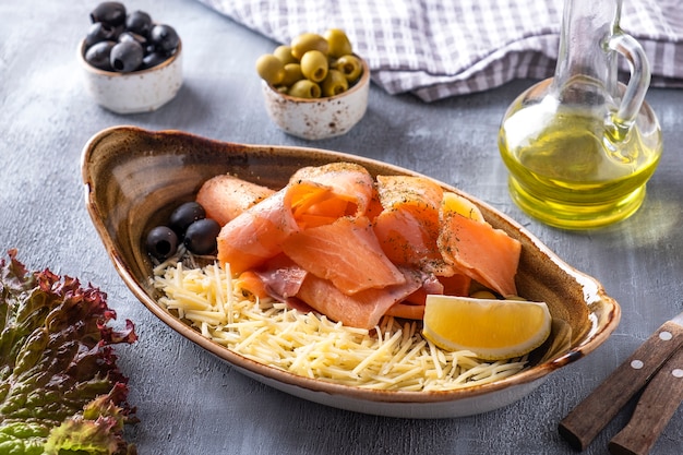 Rauwe bevroren zalm - stroganina. Rauwe bevroren vis met kaas, citroen en olijven op een bord.