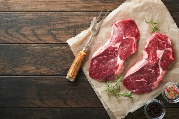 Rauwe biefstuk Gemarmerde rauwe verse Ribeye steak met rozemarijn zout en peper op snijplank op donkere betonnen achtergrond Rauwe biefstuk en kruiden om te koken