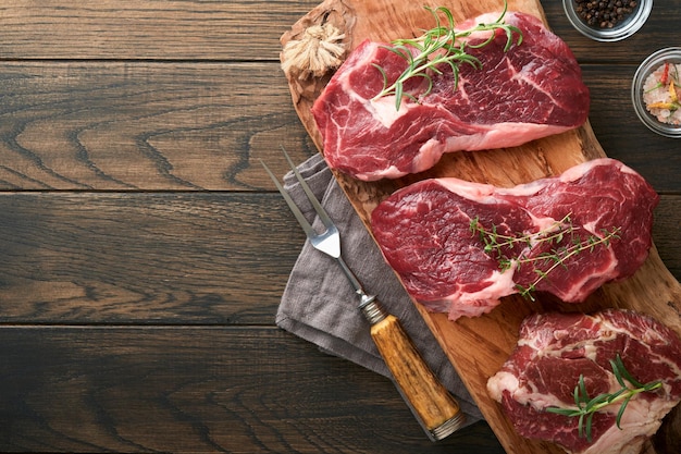 Rauwe biefstuk Gemarmerde rauwe verse Ribeye steak met rozemarijn zout en peper op snijplank op donkere betonnen achtergrond Rauwe biefstuk en kruiden om te koken