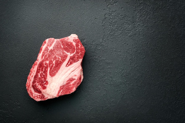 Rauwe biefstuk Rauwe verse Chuck roll steak met rozemarijn zout en peper op snijplank op donkere betonnen achtergrond Rauwe biefstuk en kruiden om te koken