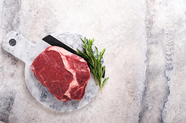 Rauwe biefstuk Vers rundvlees rib eye steak met vork rozemarijn zout en peper op marmeren stand op grijze stenen achtergrond bovenaanzicht Mockup voor ontwerpidee