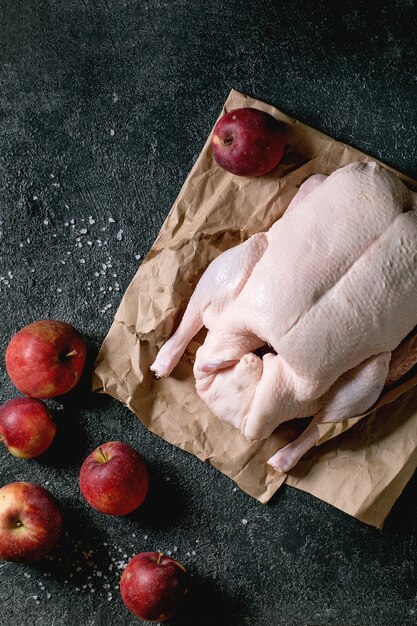 Rauwe biologische ongekookte jonge hele eend op verfrommeld papier met zout en tuinieren van rode appels rond over zwarte textuur achtergrond. Bovenaanzicht